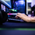 Main d'une personne utilisant un clavier de jeu devant un écran d'ordinateur.